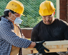 Woman and man in hard hats moving pile of wood.